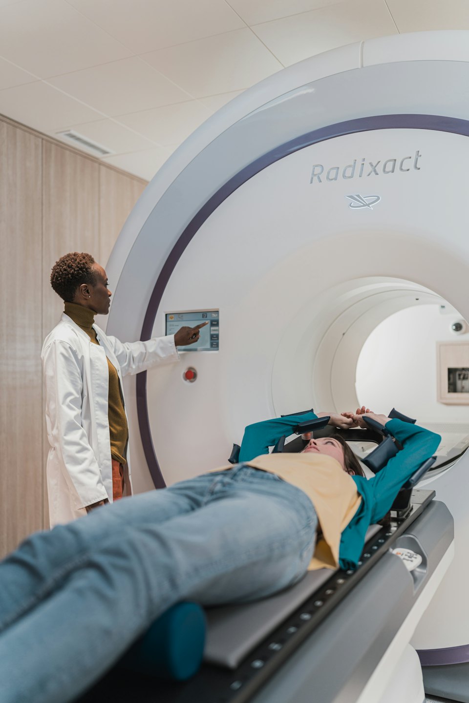 Doctor points at Radixact machine screen with patient on bed.